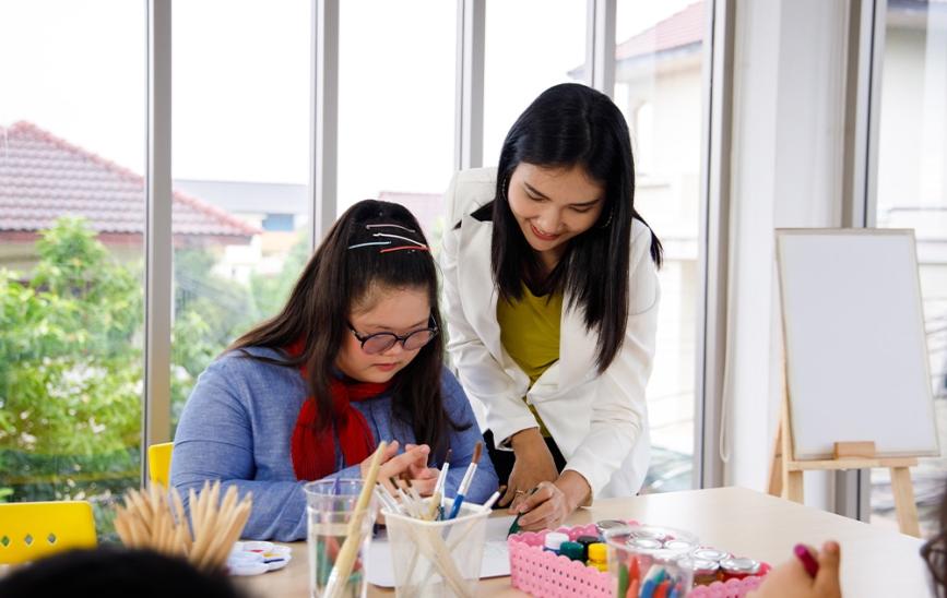 A young art teacher helps a special needs student with a project